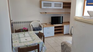 Una habitación compacta con una mesa de comedor, una silla, televisor, refrigerador y microondas.