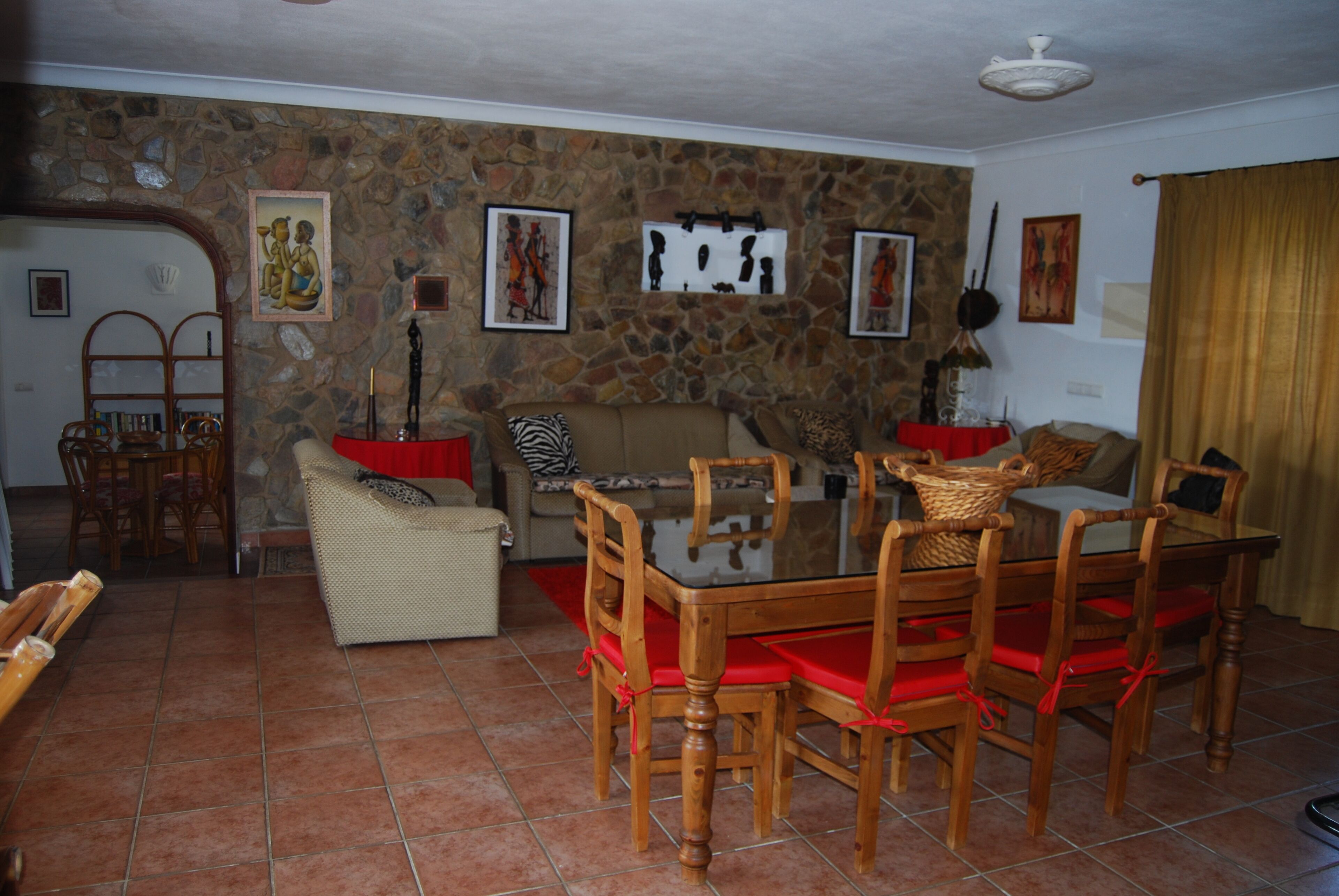 Un coin repas avec un mur en pierre, une table en bois avec des coussins rouges et un canapé.