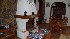Una sala de estar acogedora con una pared de piedra, una chimenea, una mesa de comedor con sillas y una mesa de centro.