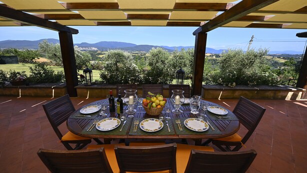 An outdoor dining area with a table set for four, surrounded by chairs, and a view of a rural landscape with mountains in the distance.