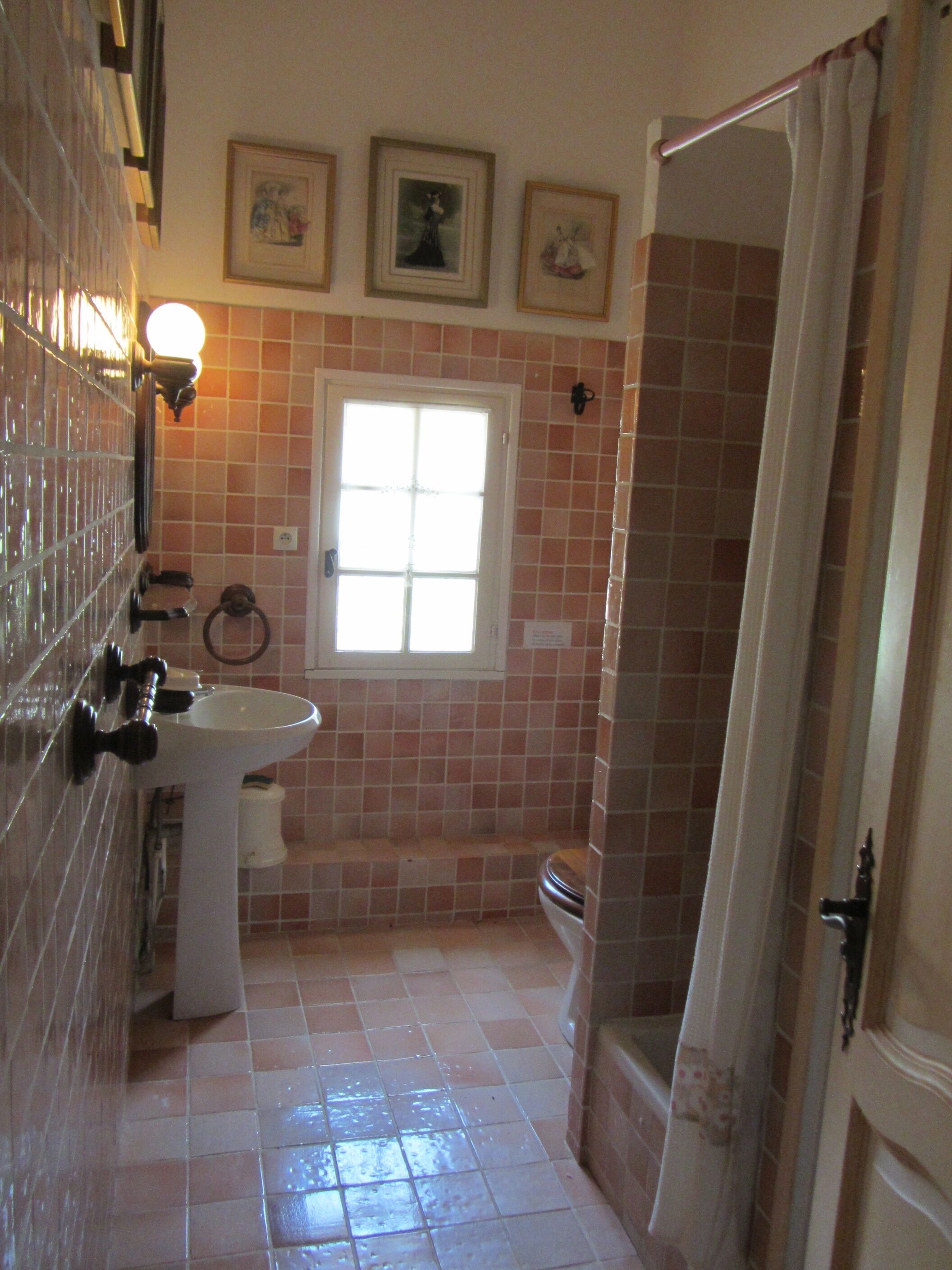 Ein Badezimmer mit Waschbecken, Toilette und Dusche. An der Wand hängen drei gerahmte Bilder.