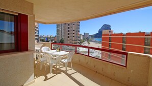 A balcony with a table and chairs, overlooking a beach and buildings.