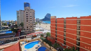 A hotel with a pool area, a beach view, and a prominent rock formation in the background.