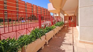A corridor with a red metal fence, potted plants, and a building with the word "OCEAN" on it.