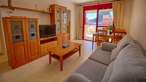 A living room with a sofa, a TV, wooden cabinets, and a dining area with a table and chairs.