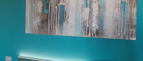 A room with a teal wall, a large abstract painting, and a curved bed with LED lights.