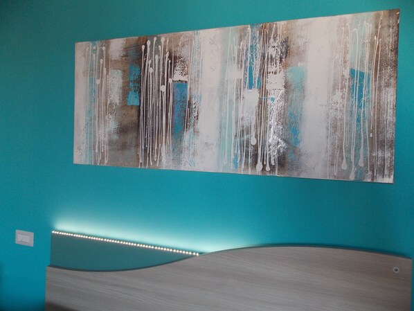Una habitación con una pared verde azulado, un cuadro abstracto grande y una cama curvada con luces LED.