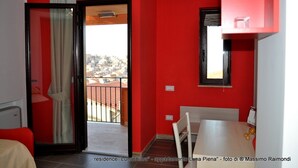 A red-walled room with a balcony, a white table, and a chair. - Apartment "Full Moon" (Tusa)