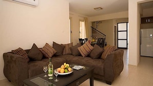 A living room with a brown sofa, a coffee table with a fruit bowl and wine glasses, and a kitchen in the background. - Villa Chrisanthi 300m from Coast Free (Coral Bay)