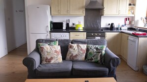 A compact living space with a kitchenette, grey sofa with patterned cushions, and a wooden dining table. - Stunning quiet location with views across the Moray Firth home to dolphins. (Rosemarkie)