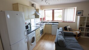 A compact kitchen with a washing machine, a refrigerator, and a dining area with a sofa and a small table. - Stunning quiet location with views across the Moray Firth home to dolphins. (Rosemarkie)