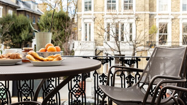 Una mesa con pasteles, un cuenco de naranjas y un frasco de mermelada en un balcón con vista a un edificio histórico.