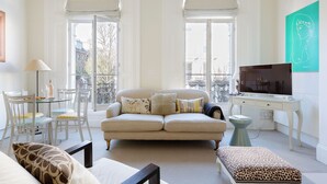 Una sala de estar con sofá, una mesa de comedor con sillas, televisor y ventana con cortinas.