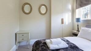 Habitación de hotel con cama, mesita de noche, lámpara y dos espejos colgados en la pared.