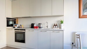 Una cocina moderna con armarios blancos, horno empotrado, cafetera y hervidor.