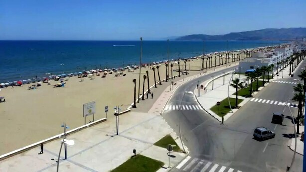 Eine Küstenstraße mit Strand auf der einen Seite und einer Reihe von Gebäuden auf der anderen.