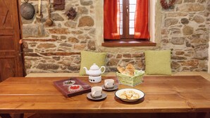 Een houten tafel met een theepot, kopjes, een schaal gebak en een mand brood.