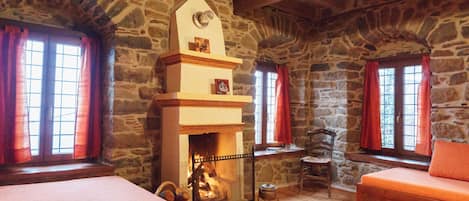 A rustic room with a stone wall fireplace, wooden beams, and a cozy seating area.