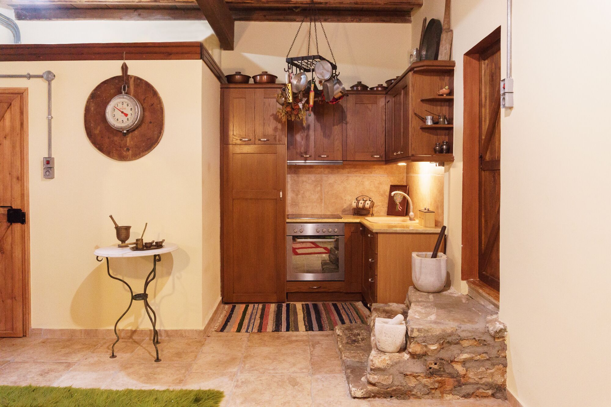 A rustic kitchen with wooden cabinets, a stove, and a hanging pot rack.