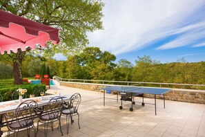 Eine Terrasse im Freien mit Tischtennisplatte, Stühlen und einem Essplatz.