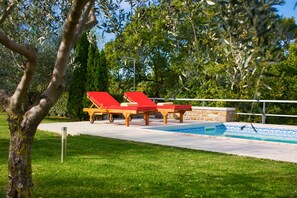 Ein Poolbereich mit zwei roten Liegestühlen und einem klaren, blauen Pool.