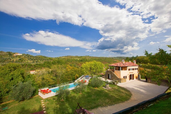 Eine Villa mit Swimmingpool, umgeben von üppiger Vegetation und Hügeln.