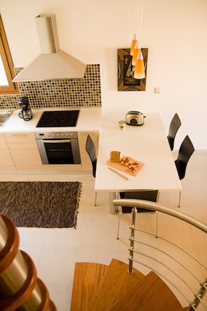 Una cocina moderna con encimera blanca, electrodomésticos de acero inoxidable y una zona de comedor con mesa blanca y sillas negras.