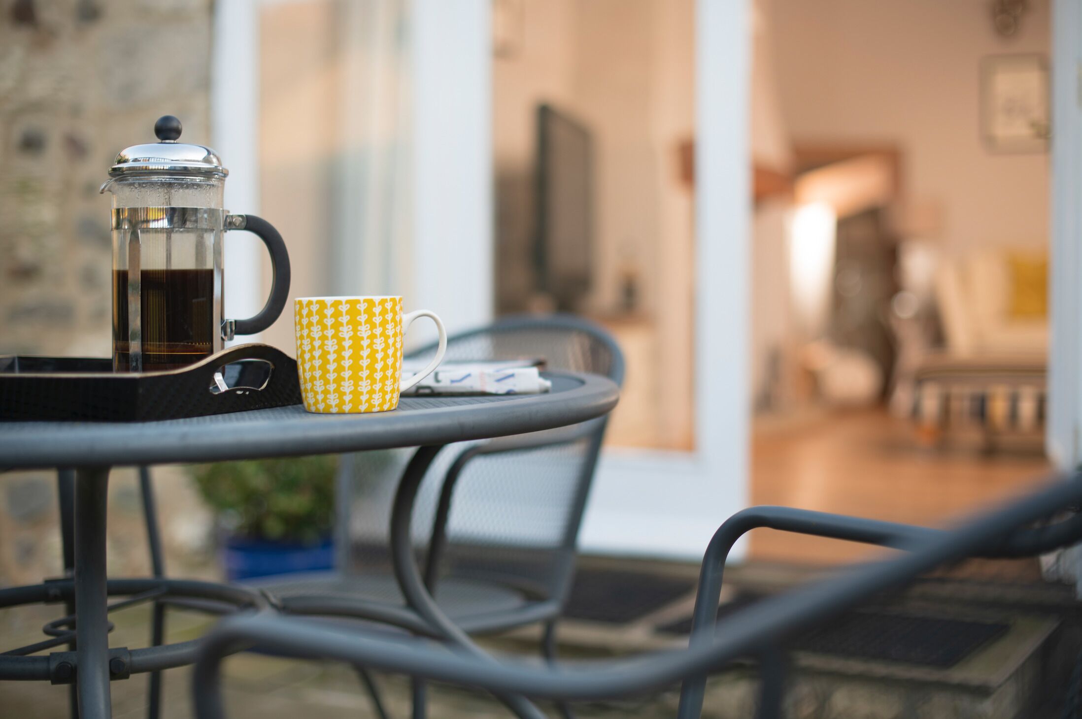 Een koffiepot en een mok met patroon op een metalen tafel met een stoel.