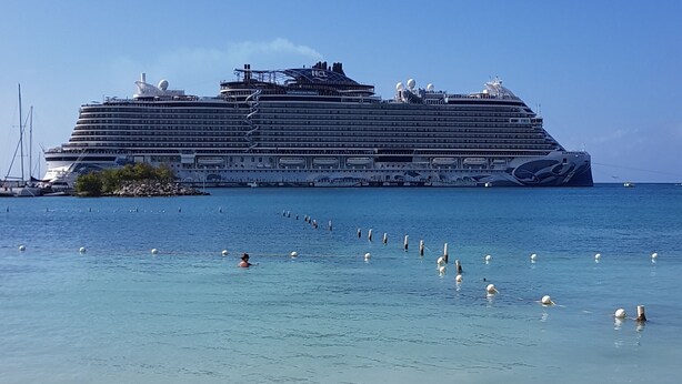 Un gran crucero amarrado en una playa con aguas turquesas cristalinas y una orilla de arena.