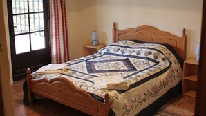 Een slaapkamer met een houten bed, een raam met gordijnen, een hanglamp en een betegelde vloer.