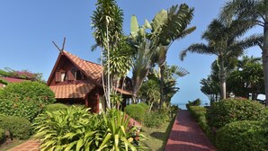A bungalow with a red tiled roof, surrounded by lush greenery and a paved pathway leading to the sea. - 3 bed beach front villa (Koh Samui)