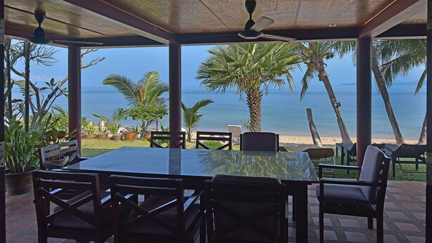 An outdoor dining area with a table and chairs, overlooking a beach and the sea. - 3 bed beach front villa (Koh Samui)