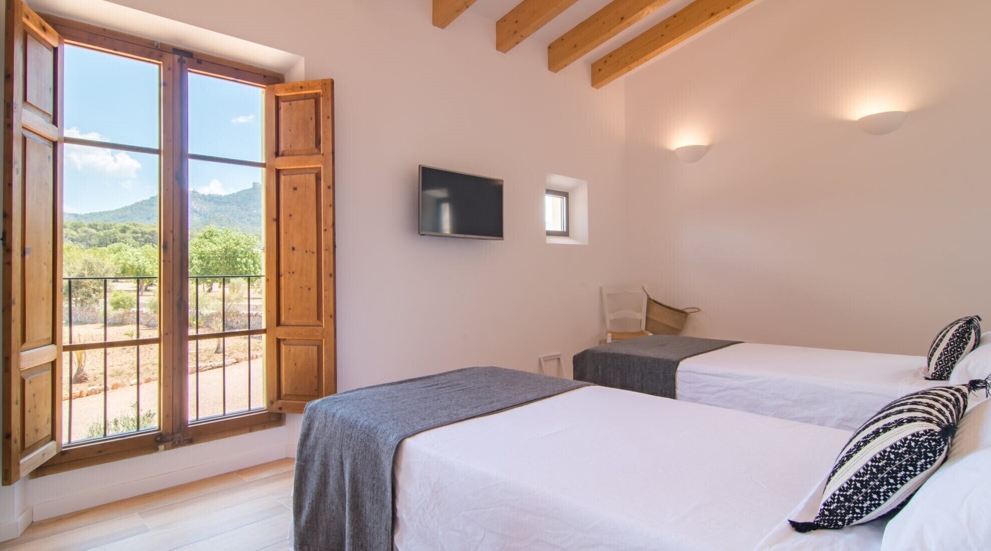 A bedroom with two beds, a TV, and a window with a view of greenery.