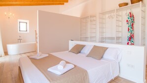 Un dormitorio con cama, un armario blanco, un baño con bañera y una araña.