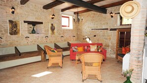 Una habitación rústica con paredes de piedra, vigas de madera, muebles de mimbre y un sofá rojo.