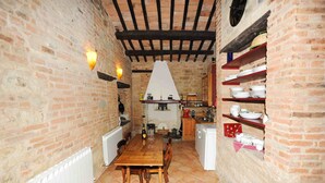 Una cocina rústica con paredes de ladrillo visto, una mesa de madera y estantes con vajilla.