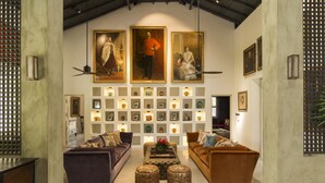 A spacious living room with a high ceiling, featuring a central coffee table, two sofas, and a decorative wall with framed artwork and shelves.