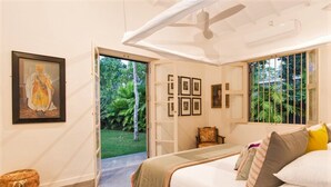 A bedroom with a bed, a chair, a framed picture, and a doorway leading to a garden.