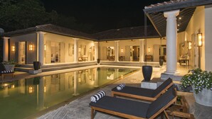A poolside area with lounge chairs, a pool, and a covered patio with columns.