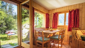 A wooden cabin interior with a dining area, a sofa, and a sliding glass door leading to an outdoor patio. - Chalet Cuckoo, Romantic Alpine Getaway. Val d'Anniviers, Valais, Switzerland (Ayer)