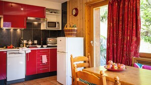 A compact kitchen with red cabinets, a white refrigerator, and a wooden dining table with a bowl of fruit. - Chalet Cuckoo, Romantic Alpine Getaway. Val d'Anniviers, Valais, Switzerland (Ayer)