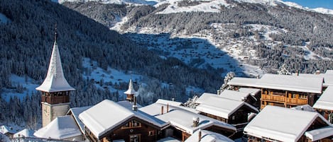 A snow-covered village with wooden buildings, a church tower, and a mountain backdrop.