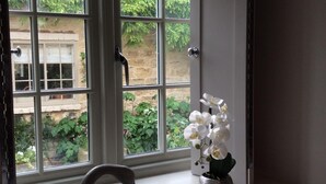 Een kamer met een raam, een witte vaas met witte bloemen, en een stenen beeldje op de vensterbank.