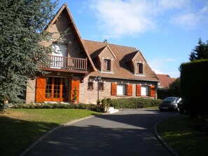 A traditional brick house with a steeply pitched roof, a front porch, and a driveway leading to a parked car. - rental room host or student or trainee (Dainville)