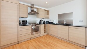 Una cocina moderna con armarios de madera clara, electrodomésticos de acero inoxidable y encimera negra.
