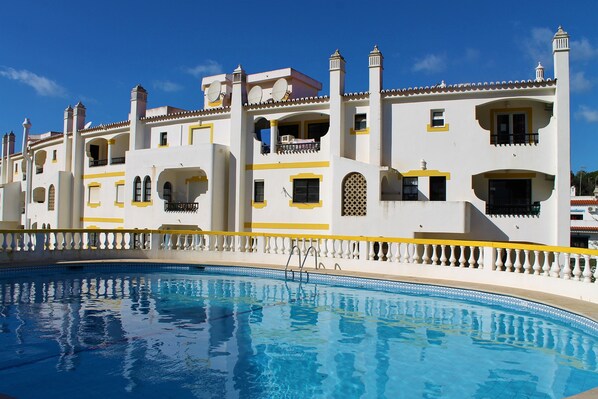 A large swimming pool with a white and yellow building in the background.