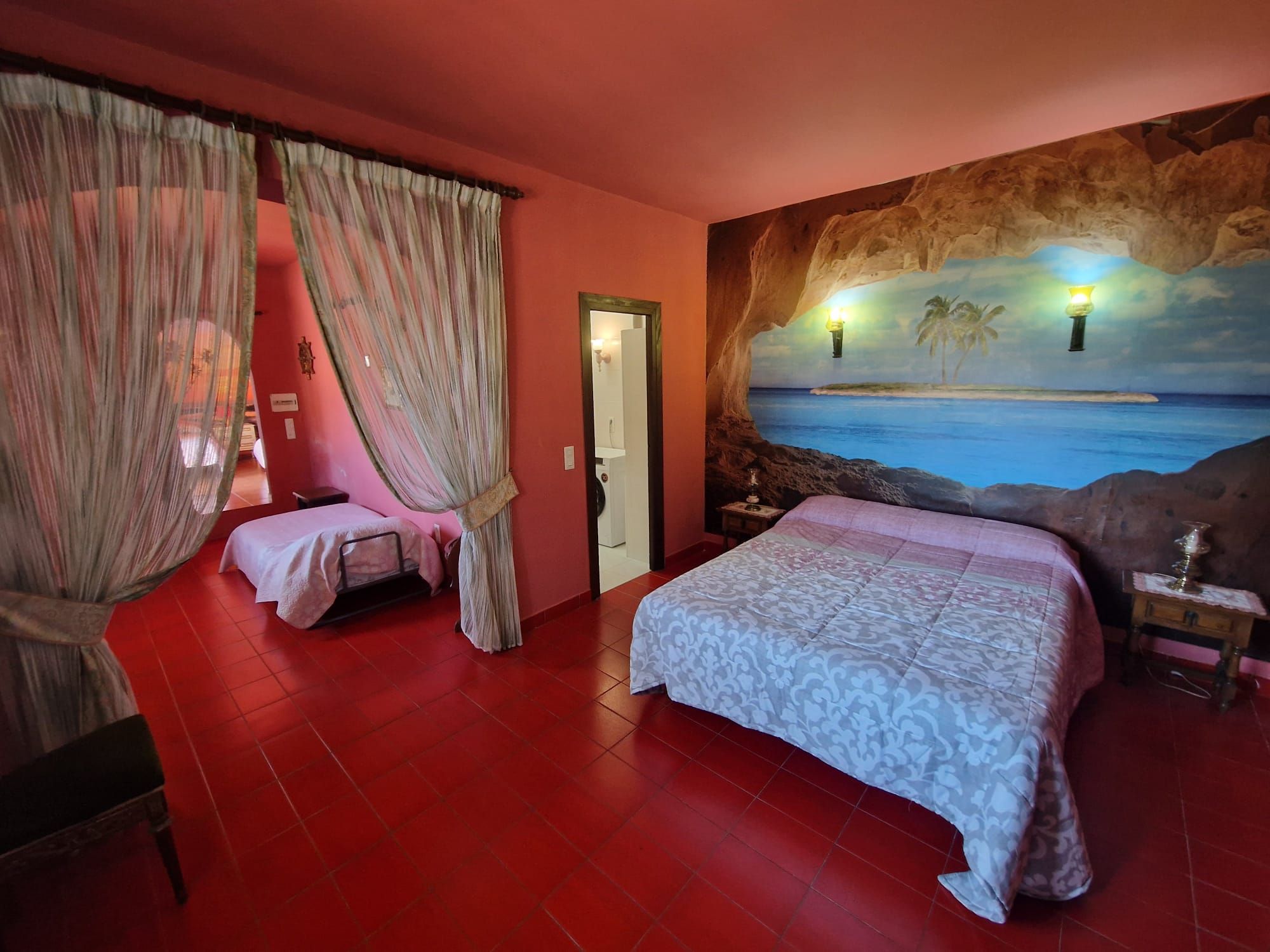 Una camera da letto con un letto grande, un letto più piccolo e un affresco raffigurante una spiaggia.
