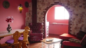 A cozy living room with a dining area, a red sofa, a wooden dining table with chairs, and a stone wall with an archway. - chalet bougainvillea sea view 500 m. from the beach available wifi (Almuñécar)
