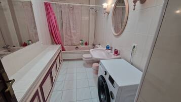 Casa de banho com banheira, sanita, lavatório e máquina de lavar roupa.