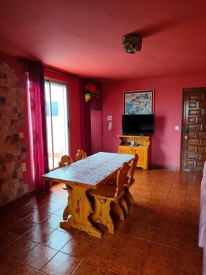 A dining area with a wooden table and chairs, a television on a wooden cabinet, and a red wall with a painting. - chalet bougainvillea sea view 500 m. from the beach available wifi (Almuñécar)